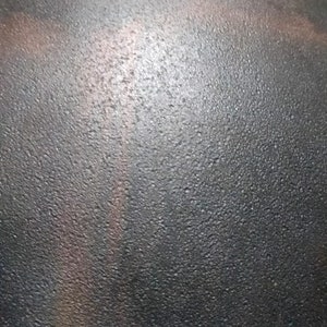 May include: A dark grey, textured, dome-shaped helmet with two metal rivets. The helmet has a subtle, iridescent sheen.