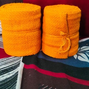 May include: Two orange fabric rolls tied with string, sitting on a colourful patterned fabric.