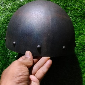 May include: A dark grey metal helmet with a rounded top and a slightly textured surface. The helmet has four small metal rivets around the edge.