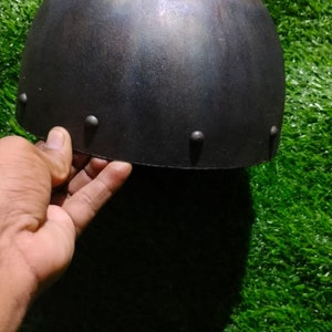 May include: A black metal helmet with a rounded top and a slightly textured surface. The helmet has several small metal rivets around the edge.