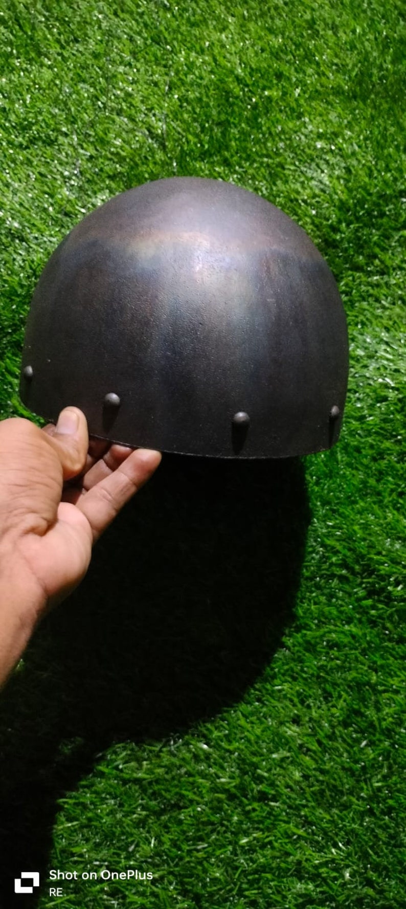 May include: A black metal helmet with a rounded top and a slightly textured surface. The helmet has several small metal rivets around the edge.