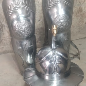 May include: A set of silver-coloured Roman gladiator armour, including two greaves with a Medusa head design and a helmet with a crest.