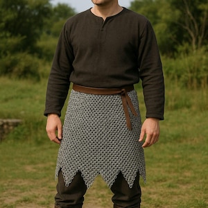 May include: A person wearing a black long-sleeved shirt with a brown leather belt and a chainmail skirt. The skirt is a pointed, asymmetrical design. The person is standing in a grassy field.