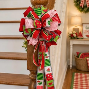 May include: A decorative bow made of multiple ribbons featuring watermelon patterns, red, green, pink, and white colors, and black and white checkered edges. The bow has a full, layered design with two long, trailing ribbon tails hanging down.