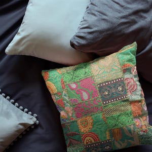 May include: An assortment of decorative throw pillows in various colors and textures. A vibrant green patchwork pillow with floral patterns is the focal point. Other pillows include a light blue, gray, and a gray pillow with pom-pom trim.