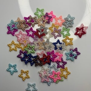 May include: A collection of colorful pearl star-shaped embellishments. The stars are made of small pearls in various colors, including pink, blue, green, purple, red, and gold.