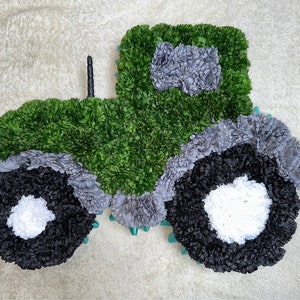 May include: A green tractor made of green, grey, black, and white tissue paper. The tractor has two large wheels and a smaller wheel at the front.