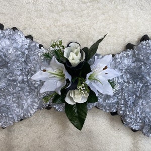 May include: A silver floral arrangement in the shape of a spanner with white lilies and roses in the centre.