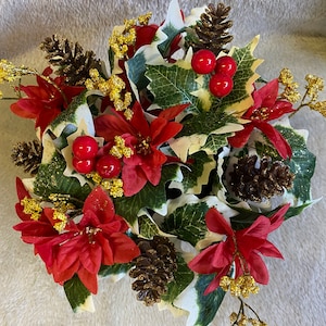 May include: A Christmas centrepiece featuring red poinsettia flowers, green holly leaves, brown pine cones, and red berries.