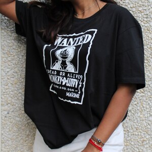 May include: Black t-shirt with a white graphic featuring the text "WANTED" and an illustration of a character. The text "DEAD OR ALIVE? MONKEY-D-LUFFY" is also visible, along with a monetary value and the word "MARINE".