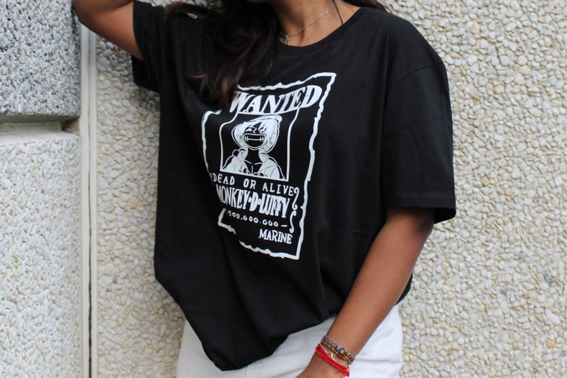 May include: Black t-shirt with a white graphic featuring the text "WANTED" and an illustration of a character. The text "DEAD OR ALIVE? MONKEY-D-LUFFY" is also visible, along with a monetary value and the word "MARINE".