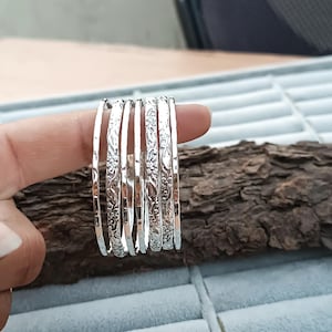 Op de afbeelding: Set zilveren armbanden met bloemenmotieven. De armbanden zijn op elkaar gestapeld.