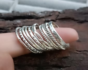 May include: A collection of silver rings with various textures, including twisted rope, beaded, and smooth bands. The rings are stacked on a finger, showcasing the different designs and the reflective quality of the metal. The rings are a mix of sizes and styles.