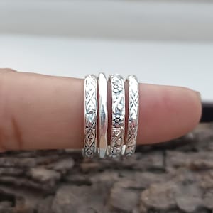 Könnte beinhalten: Satz von vier silbernen Stapelringen mit filigranen Mustern. Die Ringe werden an einem Finger getragen.