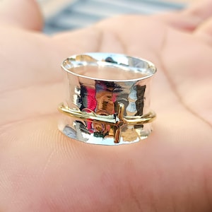 Könnte beinhalten: Ein drehbarer Ring aus Silber und Gold mit gehämmerter Oberfläche und einem Kreuzdesign.