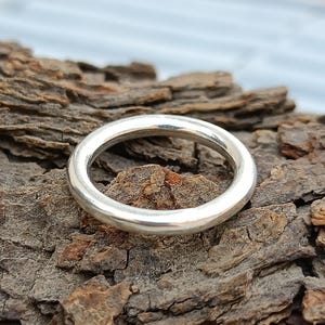 Könnte beinhalten: Ein polierter Silberring mit einem glatten, abgerundeten Design. Der Ring ist kreisförmig und scheint aus Metall gefertigt zu sein. Der Ring wird auf einer strukturierten, braunen Oberfläche präsentiert, was einen Kontrast zwischen dem glänzenden Metall und dem rauen Hintergrund erzeugt.