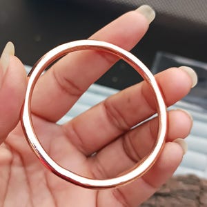 May include: A rose gold bangle bracelet. The circular bracelet is smooth and polished, reflecting light. The jewelry is held in a hand, showcasing its simple, elegant design. This accessory is suitable for everyday wear or special occasions.