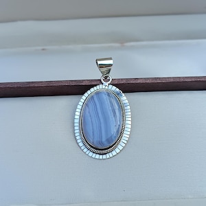 May include: A silver pendant with a light blue agate stone set in an oval frame. The stone has white and gray stripes.