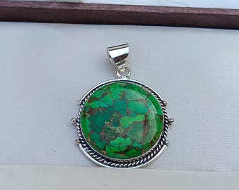 May include: A silver pendant with a round green turquoise stone set in a silver bezel. The pendant has a rope-like border and is attached to a silver bail.