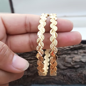 Op de afbeelding: Twee gouden armbanden met een bladontwerp. De armbanden zijn op elkaar gestapeld.