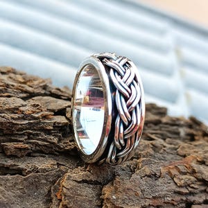 May include: A silver ring with a braided design. The ring is made of smooth, polished metal and has a simple, elegant style.