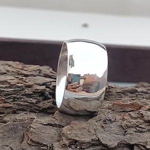 May include: A silver ring with a rounded, polished surface. The ring is reflecting the surrounding environment.