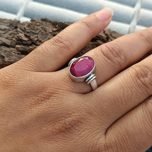 Puede incluir: Un anillo de plata con una piedra preciosa grande, de forma ovalada, de color rojo intenso. El anillo está en el dedo de una persona.