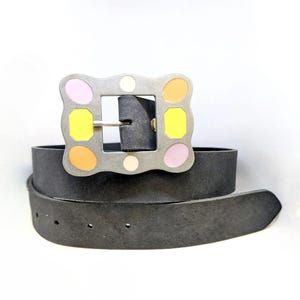 Peut inclure: Une ceinture en cuir noir avec une boucle argentée ornée d'un motif coloré de cercles roses, jaunes et oranges.