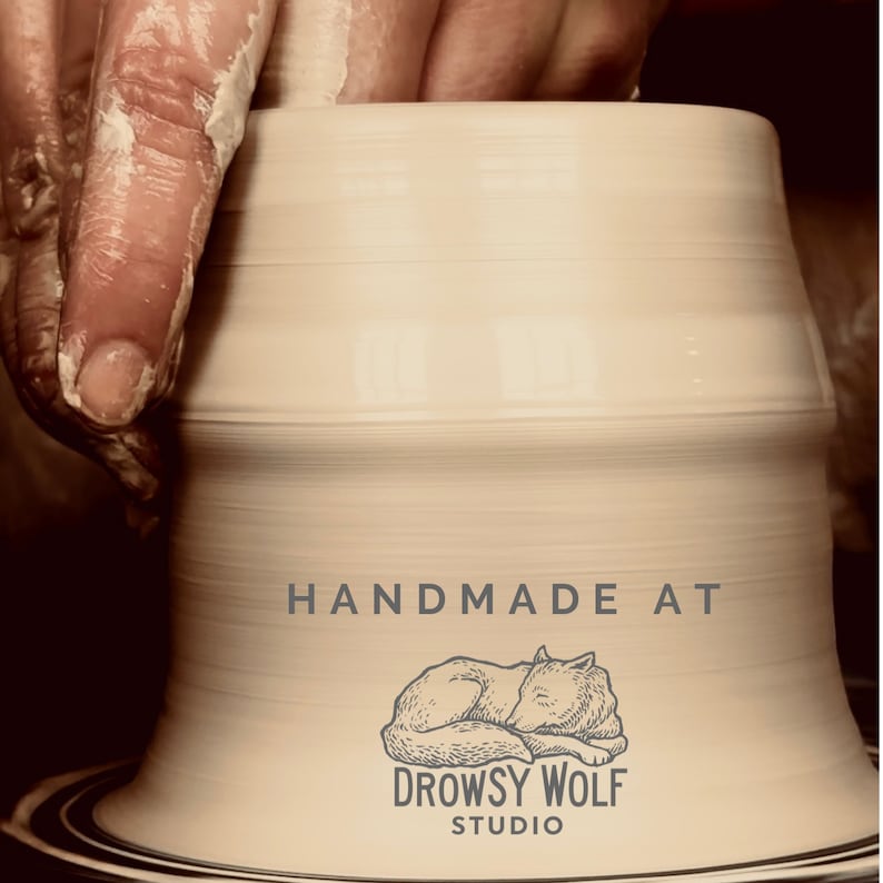 May include: A potter's hands shaping a light beige ceramic piece on a pottery wheel. The text "HANDMADE AT" is above a sleeping wolf illustration, with "DROWSY WOLF STUDIO" below.