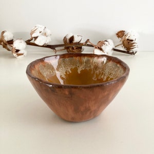 Peut inclure: Un petit bol en céramique brun avec un glaçage blanc. Le bol a une forme arrondie et un bord légèrement irrégulier.