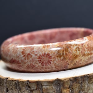 May include: A coral bangle bracelet with a polished finish. The bracelet is made of fossilized coral and features a unique pattern of red and white swirls.