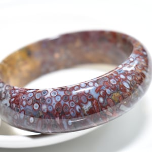 May include: A red, white, and brown agate bangle bracelet with a unique pattern of small white circles.