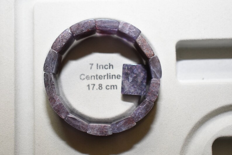 Puede incluir: Un brazalete de piedras preciosas de color p&uacute;rpura y gris con una circunferencia de 17,8 cm. El brazalete est&aacute; hecho de piedras rectangulares individuales.