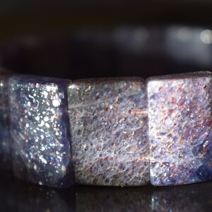 Puede incluir: Un brazalete hecho de cuentas de piedras preciosas azules y moradas iridiscentes. Las cuentas son facetadas y tienen un acabado brillante.