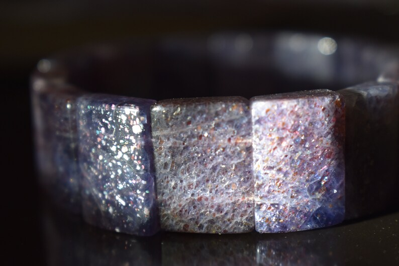 Puede incluir: Un brazalete hecho de cuentas de piedras preciosas azules y moradas iridiscentes. Las cuentas son facetadas y tienen un acabado brillante.