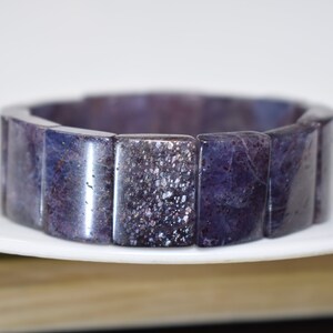 Puede incluir: Un brazalete de piedras preciosas de color morado y gris hecho de cuentas rectangulares.