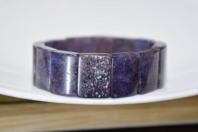 Puede incluir: Un brazalete de piedras preciosas de color morado y gris hecho de cuentas rectangulares.