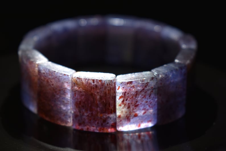 Puede incluir: Un brazalete de piedras preciosas de color p&uacute;rpura y rojo hecho de cuentas rectangulares.