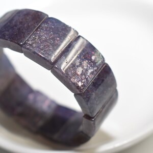 Puede incluir: Un brazalete de piedras preciosas de color morado oscuro con brillo iridiscente. El brazalete est&aacute; hecho de cuentas rectangulares y es el&aacute;stico.
