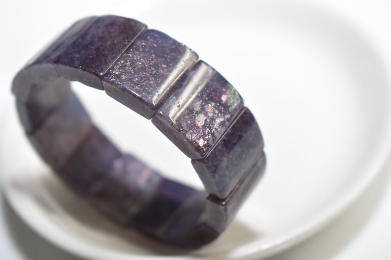 Puede incluir: Un brazalete de piedras preciosas de color morado oscuro con brillo iridiscente. El brazalete est&aacute; hecho de cuentas rectangulares y es el&aacute;stico.