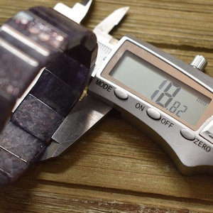 Puede incluir: Primer plano de un calibre digital que mide una pulsera de color morado oscuro. El calibre muestra 1,82 mm.
