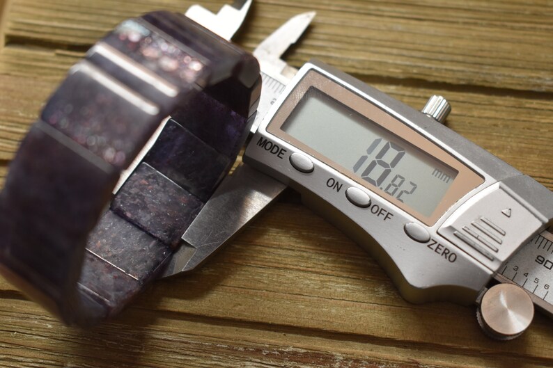 Puede incluir: Primer plano de un calibre digital que mide una pulsera de color morado oscuro. El calibre muestra 1,82 mm.