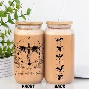 Puede incluir: Una botella de vidrio reutilizable con tapa de bambú y una pajita. La botella contiene un líquido marrón y un gráfico en blanco y negro de un dragón con el texto "No moriré hoy". La parte posterior de la botella tiene un gráfico en blanco y negro de cinco dragones.