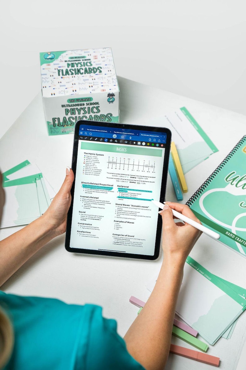 Op de afbeelding: Een close-up van een tabletscherm waarop een set natuurkunde-flashcards wordt weergegeven. Het scherm toont een sectie met de titel "Basics" met onderwerpen zoals "Het metrische stelsel", "Geluidsgolven" en "Categorie&euml;n van geluid". De tablet ligt op een wit oppervlak met een stapel flashcards en een stylus.