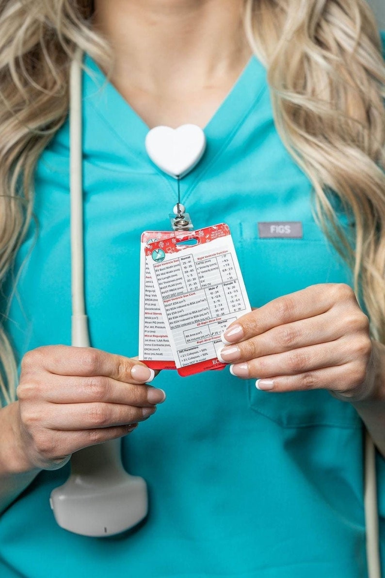 May include: A red and white card with a chart of medical information. The card is labeled "Right Ventricular Function" and includes measurements for various parameters. The card is held by a person wearing a blue medical scrub top with a heart-shaped badge.
