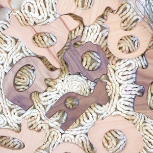 May include: A set of wooden teethers shaped like animals, including a giraffe, elephant, and other animal shapes. The teethers are made of natural wood and are perfect for babies to chew on.