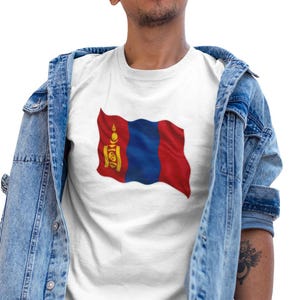 Può includere: T-shirt bianca con la bandiera della Mongolia. Il design della bandiera include colori rosso, blu e giallo. La persona nell'immagine indossa una giacca di jeans e pantaloni neri.