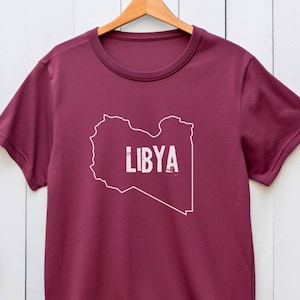 Può includere: T-shirt color borgogna con un contorno bianco del paese della Libia e la parola "LIBYA" in bianco.