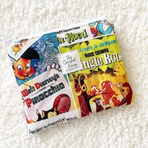 May include: A square fabric zipper pouch featuring a collage of vintage Disney movie posters including Pinocchio and The Jungle Book. A white square label in the center displays the text The Crochet Ficus Handmade Goods.