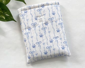 Könnte beinhalten: Eine weiße, gepolsterte Hülle mit blauem Blumen- und Bandmuster. Die Hülle hat ein gestepptes Design und ein kleines Etikett mit der Aufschrift "The Comfort Fiery". Die Hülle ist für ein Tablet oder einen E-Reader konzipiert.